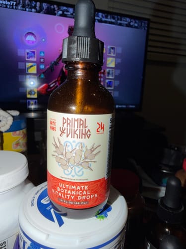 Reviewer's bottle of Libido Fire Drops sitting on a desk in front of a computer screen.