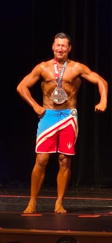 A reviewer with a toned, muscular physique posing on a competition stage.