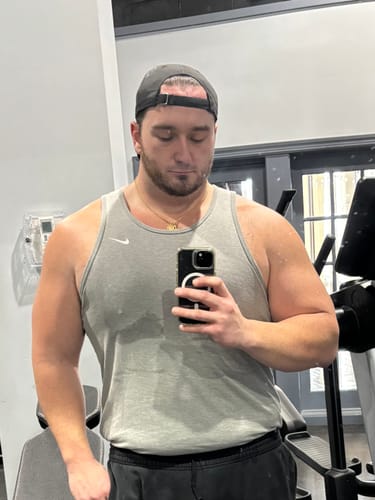 Reviewer in a grey tank top takes a selfie in a gym setting.